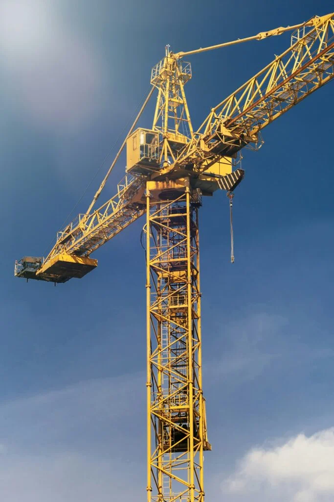 Construction crane tower in sun light beams on background of blue sky